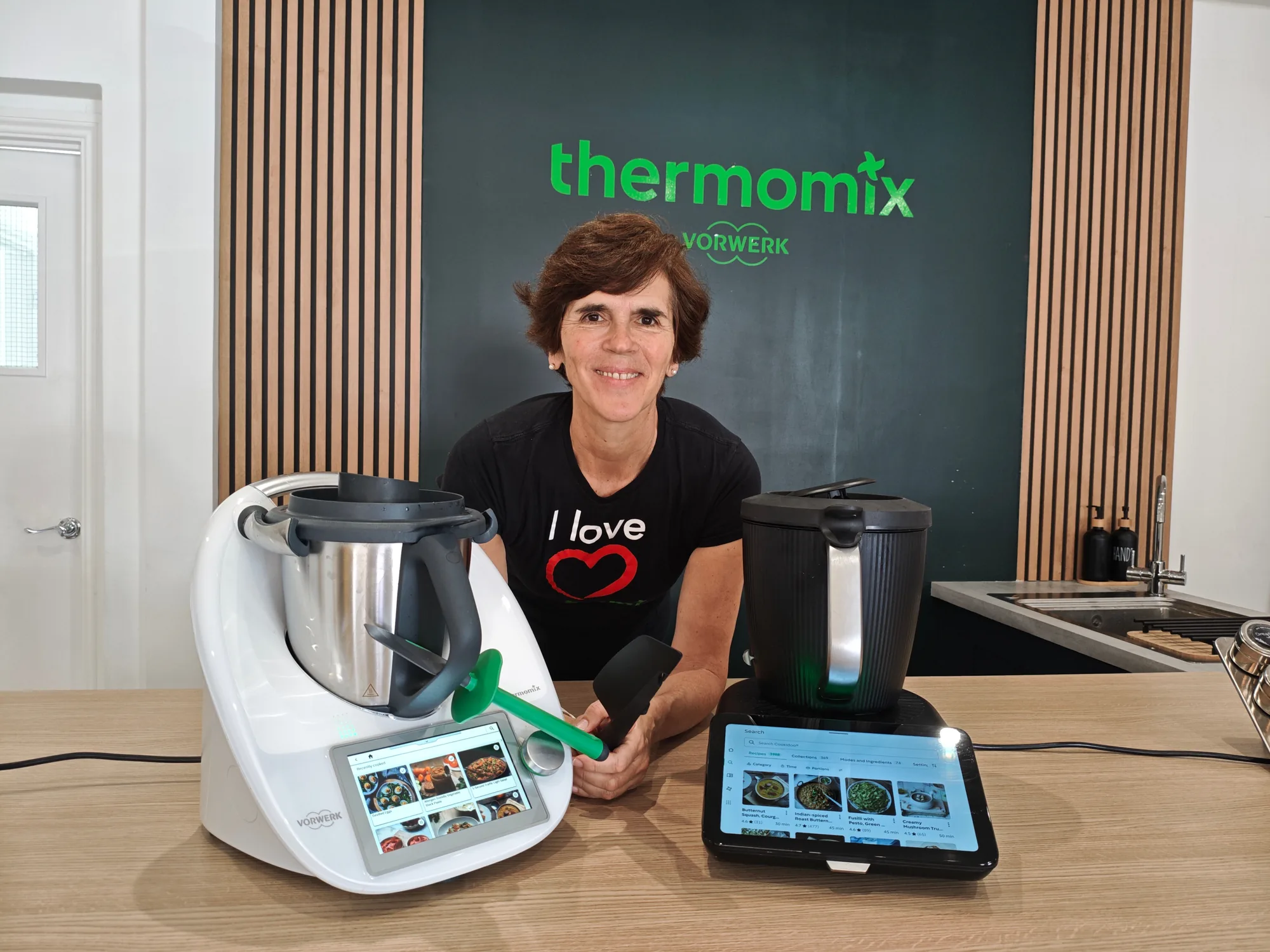 A Thermomix TM6 and a Thermomix TM7 side by side on the same worktop, both switched on.